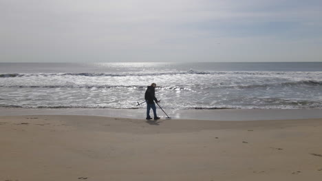 Drone-Shot-Of-Man-With-Metal-Detector-On-Empty-Beach