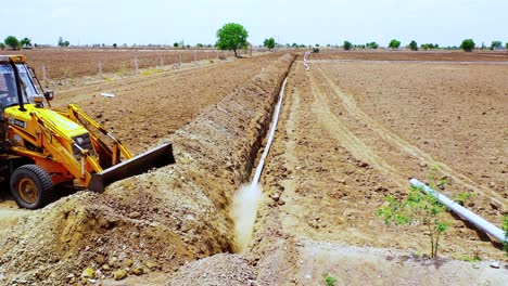 Earthmoving-machine-cover-up-water-pipeline-with-soil,-heavy-duty-excavation-machine-at-Indian-agricultural-land