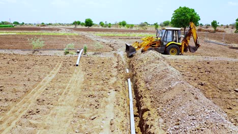 Water-pipeline-solution-in-India,-heavy-duty-excavation-machine-at-Indian-agricultural-land,-Aerial-view