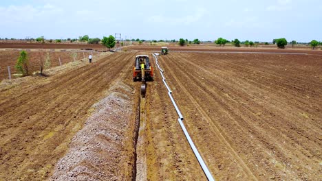 Aerial-view-of-green-tractor-unload-water-pipeline-at-farm-for-installation,-agricultural-farm