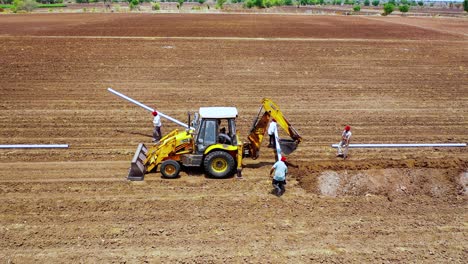 Indian-farmer-a-labor-carry-water-pipeline-for-the-fittings-at-agricultural-land,-aerial-top-down-shot