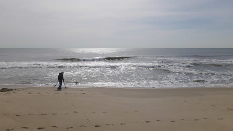 Man-Walking-With-Metal-Detector-On-Empty-Beach-In-Silhouette