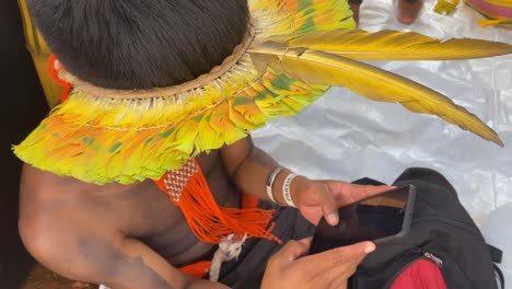 An-Amazon-indigenous-man-dressed-in-a-brightly-colored-plumed-hat-works-on-a-smartphone