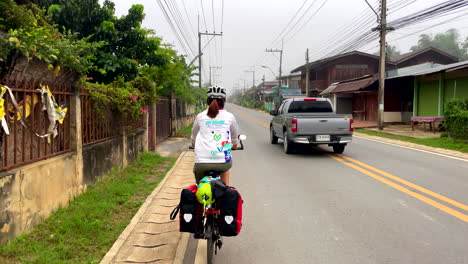 Una-Ciclista-Solitaria-Circulando-Por-Una-Carretera-Urbana-Con-Otros-Vehículos-Pasando-Por-La-Provincia-De-Nan,-Tailandia