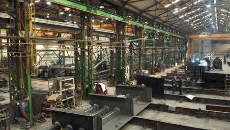 Workers-welding-steel-beams-in-steelworks-factory-manufacturing-hall