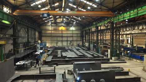Steelworks-factory-storage-hall-with-workers-welding-steel-beams,-Brno