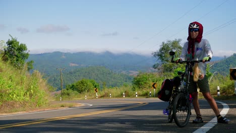 Una-Ciclista-Solitaria-Descansa-En-Una-Carretera-Cerca-De-La-Aldea-De-Pescadores-De-Paknai-Antes-De-Continuar-Empujando-Su-Bicicleta-En-El-Distrito-De-Na-Muen,-Nan,-Tailandia