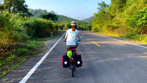 A-lone-female-cyclist-rides-along-a-road-near-Paknai's-Fisherman-Village-in-the-Na-Muen-District,-Nan,-Thailand