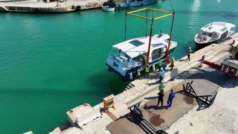Drone-aerial-shot-orbiting-around-a-boat-lifted-in-air-while-workmen-moving-it-into-the-sea-at-MMH-ship-yard-Malta