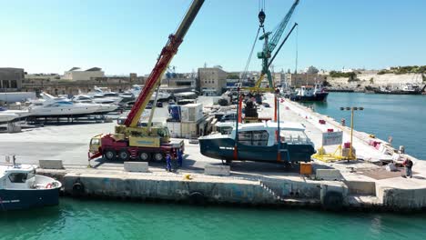 Drone-aerial-shot-flying-away-from-a-boat-being-lifted-in-air-while-moving-it-into-the-sea-at-MMH-ship-yard-Malta