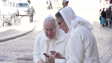 A-couple-of-old-age-nun's-scrolling-through-their-mobile-near-a-wailing-wall