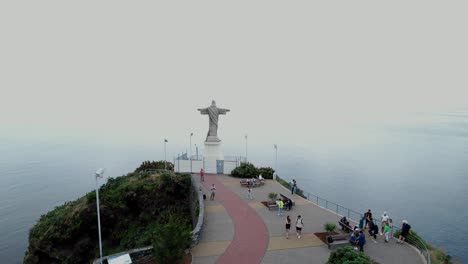 Aerial-view-orbiting-people-sightseeing-Cristo-Rei-landmark-sculpture-looking-out-across-misty-ocean