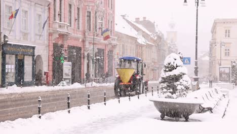 Gritter-Tractor---Winter-Service-Vehicle-Mounted-With-Salt-Spreader-Driving-In-The-Street-Of-Brasov-During-Snowfall-In-Winter