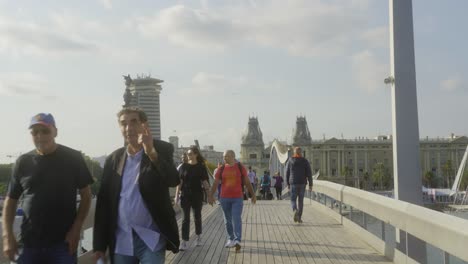 People-walking-over-bridge-Rambla-de-Mar-in-Barcelona,-Spain-on-sunny-day