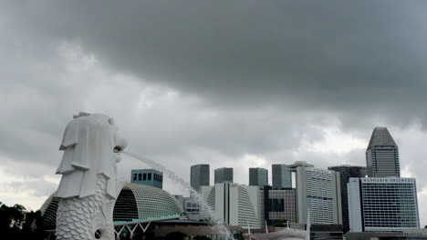 Formación-De-Nubes-Oscuras-Sobre-El-Merlion-De-Singapur-Con-Un-Edificio-Al-Fondo