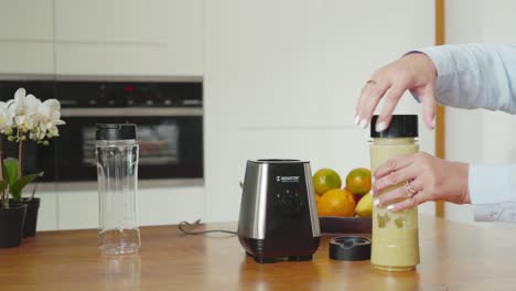 Hand-popping-bottle-out-from-mixer,-puts-on-lid-and-leaves-for-work-with-tasty-smoothie