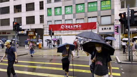 Asian-people-crossing-crosswalk-in-Wan-Chai-with-umbrellas-on-rainy-day,-Hong-Kong