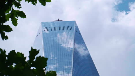 Reveal-slider-shot-behind-foliage-of-tall-One-World-Trade-Center-against-clouds