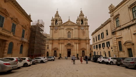 Low-angle-shot-of-tourists-visiting-St-Paul's-Cathedral-in-Mdina-,-Malta-on-a-cloudy-evening-time