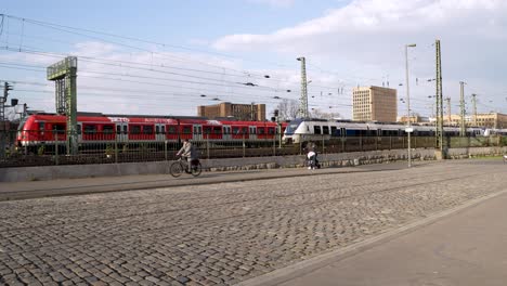 Regional-Trains-Passing-Each-Other-Beside-Cobbled-Pavement-Beside-Hohenzollern-Bridge-In-Cologne