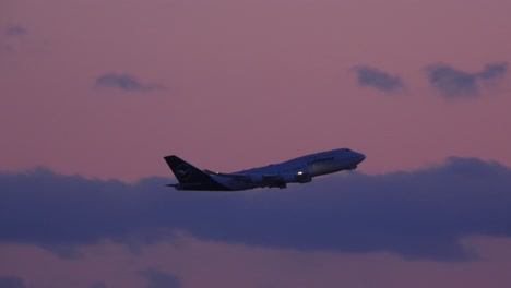 Lufthansa-passenger-plane-takes-off-as-the-sun-sets-creating-a-pink-and-purple-partly-cloudy-sky