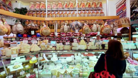 Customer-served-in-a-delicatessen-shop-with-many-types-of-ham-hanging-in-Italy