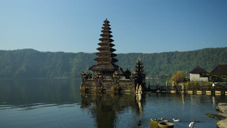 Slow-motion-panning-shot-of-Pura-Ulun-Danu-temple-with-view-of-volcanic-lake-and-surrounding-nature-with-swimming-ducks