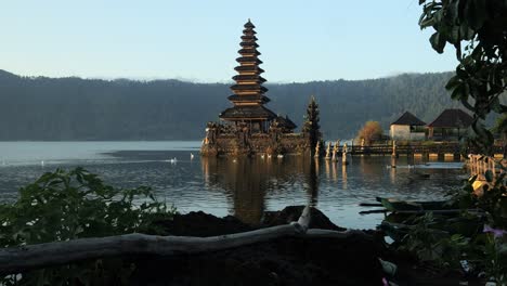 Ascending-shot-of-a-magnificent-hindu-temple-located-in-the-water-of-Pura-Segara-Ulun-Danu-at-volcano-lake-batur-during-golden-hour-and-calm-waters-reflecting-off-the-lake