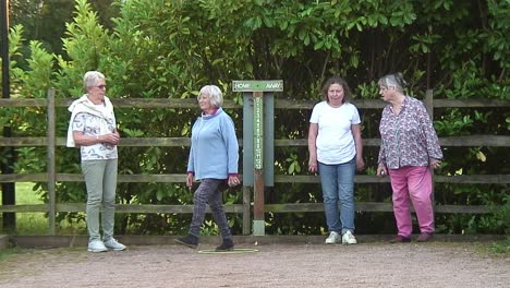 Four-ladies-competing-against-one-another-playing-the-French-sport-of-pétanque-where-they-each-toss-their-boules-at-a-small-cocoon-trying-to-get-as-close-to-it-as-possible