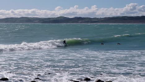 Surfers-catching-waves-in-surfing-town-of-Raglan-in-Waikato,-New-Zealand-Aotearoa