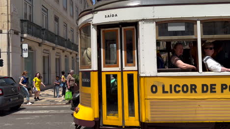 Establishing-slow-motion-of-passing-famous-yellow-tram-in-Lisbon-Downtown-during-sunny-day---traffic-on-road-with-many-people-in-pedestrian-zone