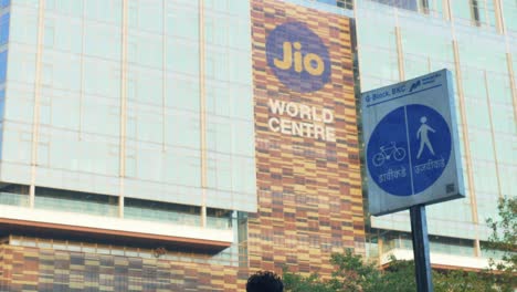 Construction-worker-talking-over-smartphone-during-break-in-front-of-Reliance-India's-largest-Convention-Centre-Jio-World-Centre-With-5G-Network,-Bandra-Kurla-Complex,-Mumbai