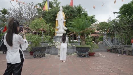Ein-Tourist,-Der-Fotos-Von-Einer-Frau-Macht,-Die-An-Der-Weißen-Statue-Der-Gottheit-Quan-Am-In-Der-Van-Son-Pagode-In-Con-Dao,-Vietnam,-Betet