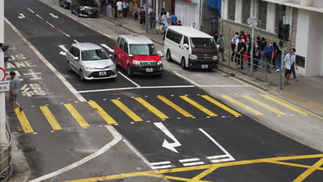 Cars-wait-at-traffic-stop-as-people-walk-on-crosswalk-and-sidewalk-in-hong-kong