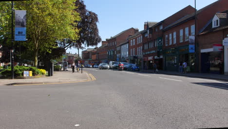 Grantham-Town-Center-High-Street-In-Summer-With-Traffic-Driving-Past-Shops-and-People-Walking-In-England