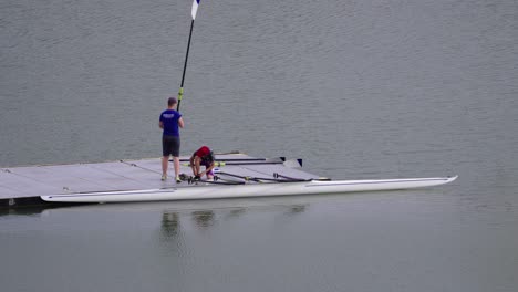 Two-young-rowers-prepare-a-double-scull-and-oars-on-a-pier-in-the-rowing-arena