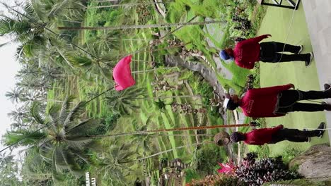 Hinter-Den-Kulissen-Eines-Mädchens-In-Einem-Langen-Roten-Schleppenkleid,-Das-Auf-Einer-Schaukel-Mit-Blick-Auf-Palmenwälder-Und-Reisfeldterrassen-In-Alas-Harum,-Ubud,-Bali,-Ein-Fotoshooting-Macht