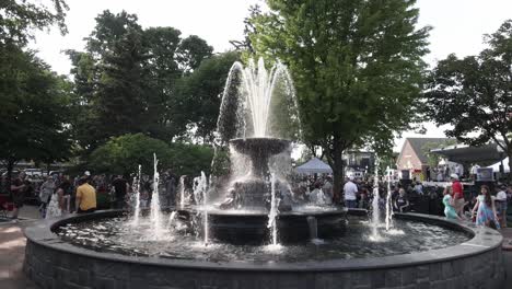 Water-fountain-and-people-gathered-at-an-outdoor-music-concert-at-Kellogg-Park-in-Plymouth,-Michigan-with-gimbal-video-walking-forward