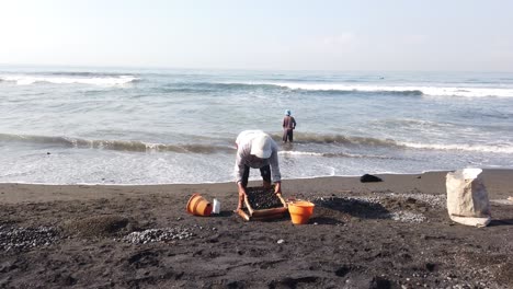 Workers-Collect-Black-Rounded-Stones-at-Beach,-Traditional-Job,-Bali-Indonesia