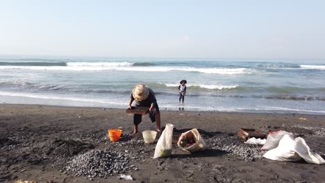 Workers-from-Indonesia-Pick-Up-Pebbles-From-Black-Sand-Beach,-Traditional-Job
