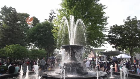 Water-fountain-and-people-gathered-at-an-outdoor-music-concert-at-Kellogg-Park-in-Plymouth,-Michigan-with-gimbal-video-tilting-down