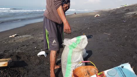 Traditional-Worker-Picks-Up-Stones-Cultural-Work-at-the-Beach-in-Bali-Indonesia,-Collecting-Pebbles