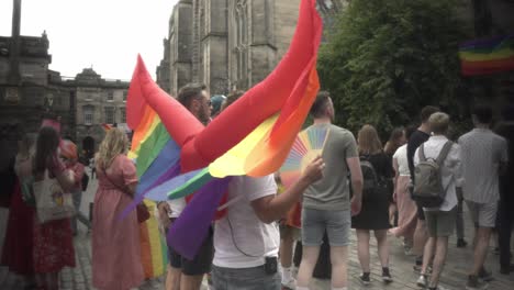 Witness-the-vibrant-spirit-of-a-man-wearing-inflatable-wings-adorned-with-the-colors-of-the-LGBTQ-flag,-proudly-participating-in-the-Pride-march-along-Edinburgh's-iconic-Royal-Mile