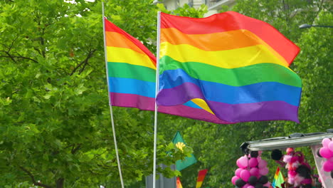 LGBT-Flaggen,-Die-Auf-Einer-Hölzernen-Laube-Gehisst-Wurden-Und-Von-Menschen,-Die-Sie-In-Ihren-Händen-Hielten,-Im-Wind-Gemäht-Wurden