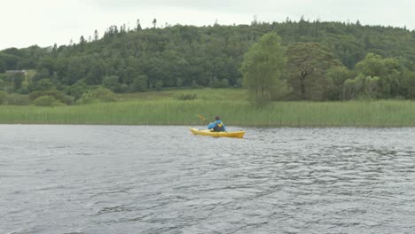 A-young-man-paddling-a-yellow-kayak-along-a-river