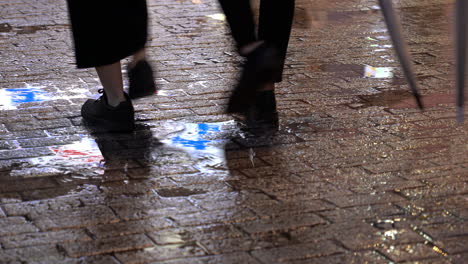 People-walking-on-brick-street-in-rainy-evening-with-sign-and-lights-are-reflected-in-a-water-puddle