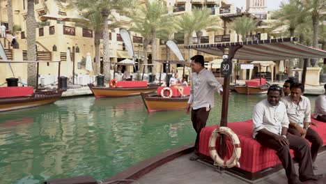 Hotel-Staffs-And-Tourists-Riding-The-Abra-Boat-In-Madinat-Jumeirah-With-Luxury-Hotels-In-Dubai,-United-Arab-Emirates