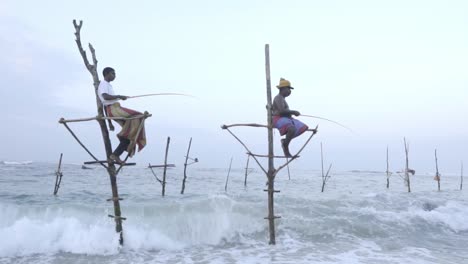 Stilt-Fishermen-Using-A-Fishing-Rod-On-Catching-Fish-With-Waves-Splashing-On-The-Coastline-In-Weligama,-Sri-Lanka