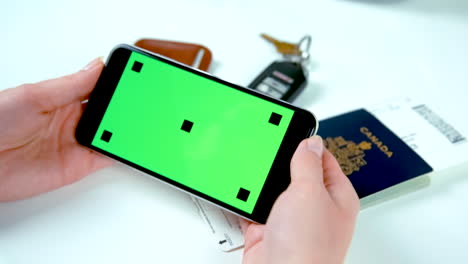 Woman's-Hands-Holding-Green-Screen-Cell-Phone-with-Canadian-Passport-in-Background---At-60-fps