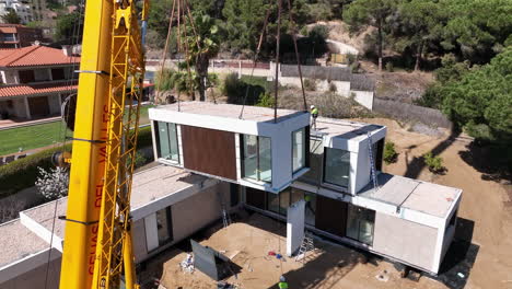 Establishing-aerial-view-of-sustainable-modular-housing-suspended-by-heavy-crane-in-assembling-suburban-real-estate-property